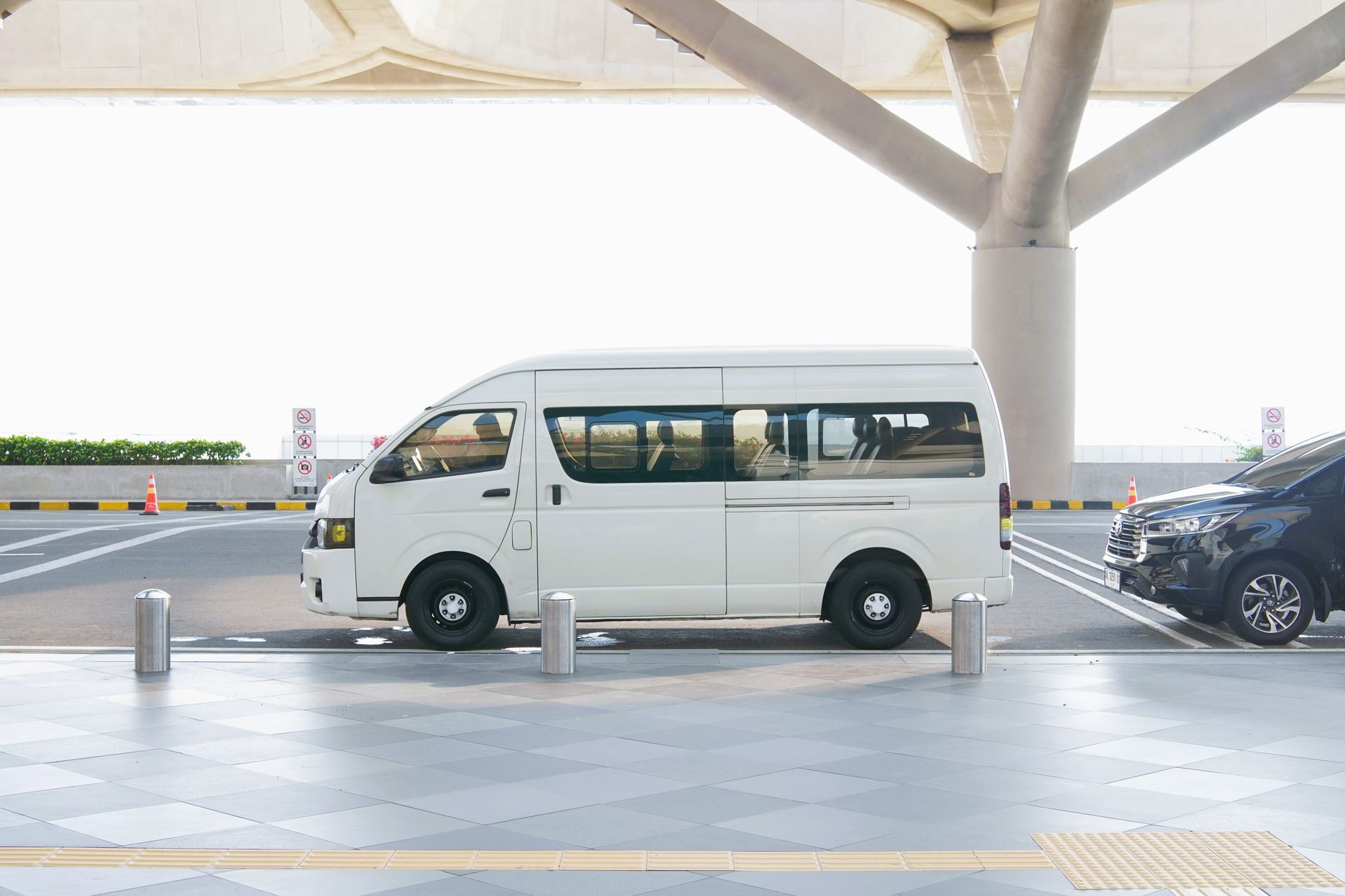 White passenger transfer minivan parked along the curbside passenger pickup lane at a modern airport terminal.