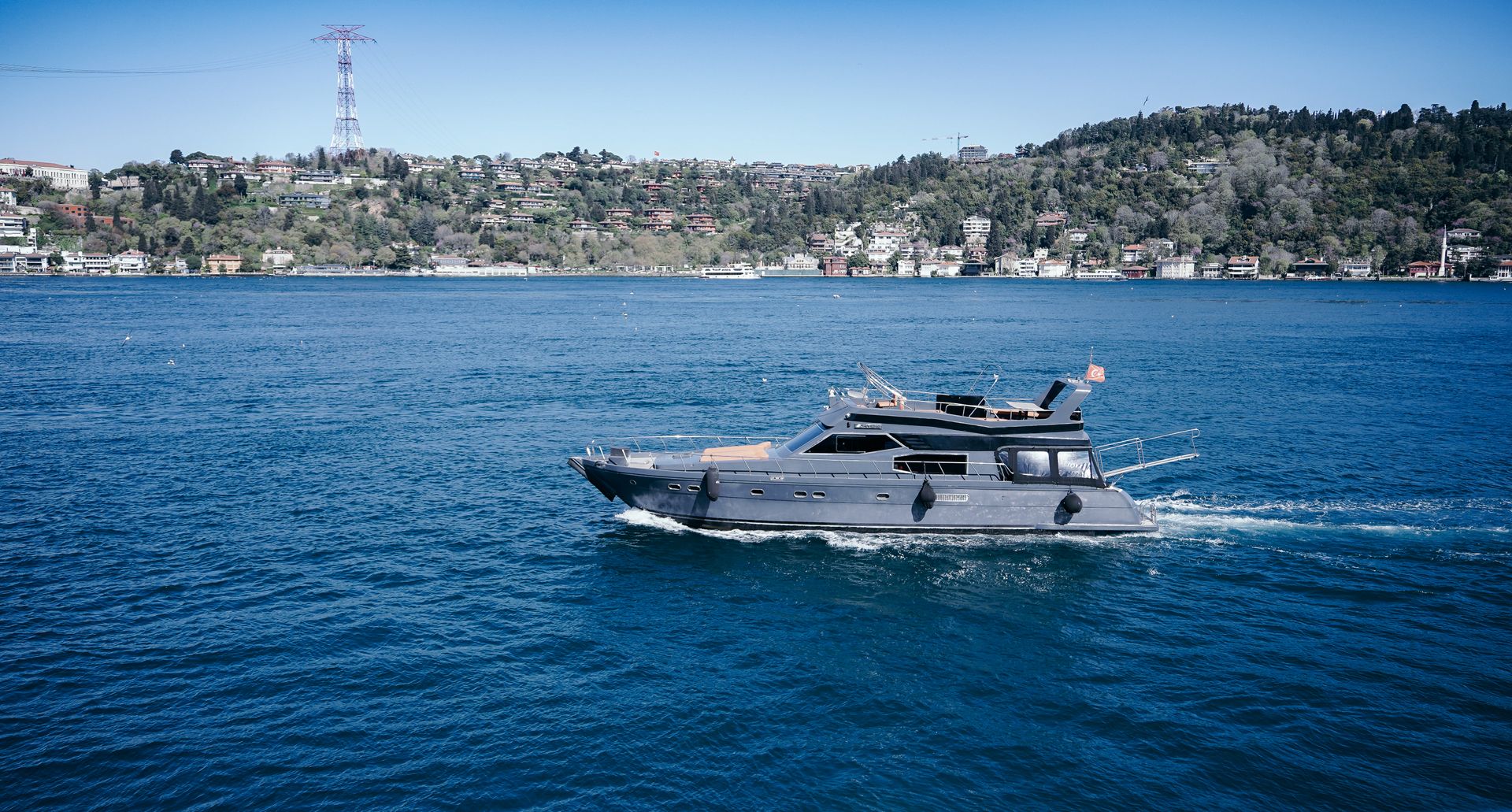 Private luxury motor yacht cruising across the blue waters of Bosphorus strait along European waterfront.