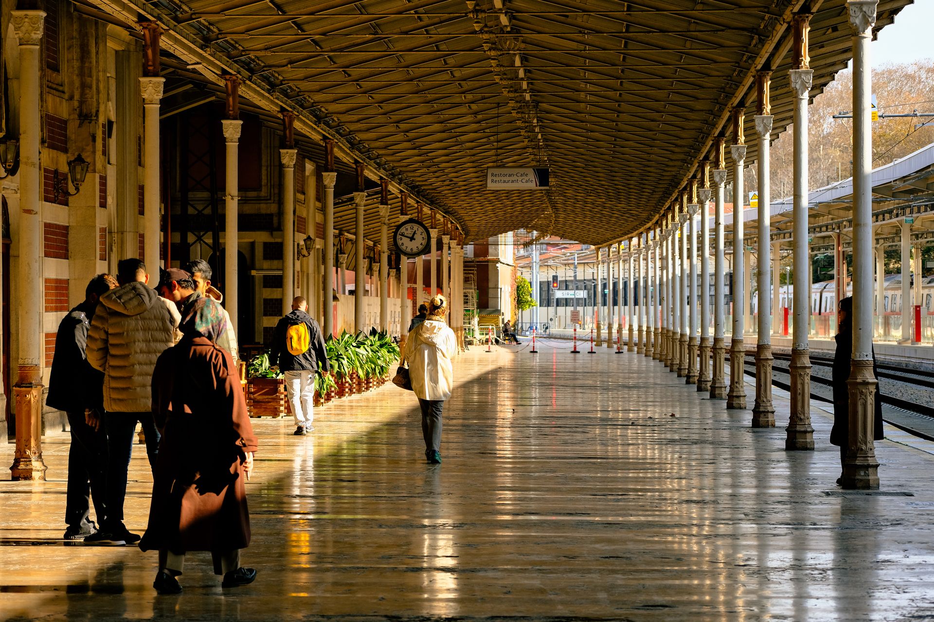 Commuters and travelers walking along the grand platforms and arched canopy of historic Sirkeci Train Station in Istanbul.