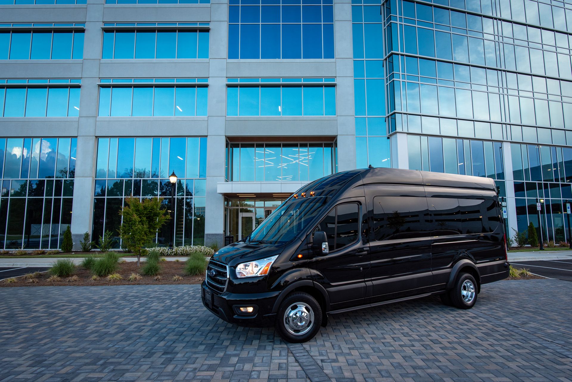 Executive black passenger minibus and transport van parked in front of a modern corporate building entrance.