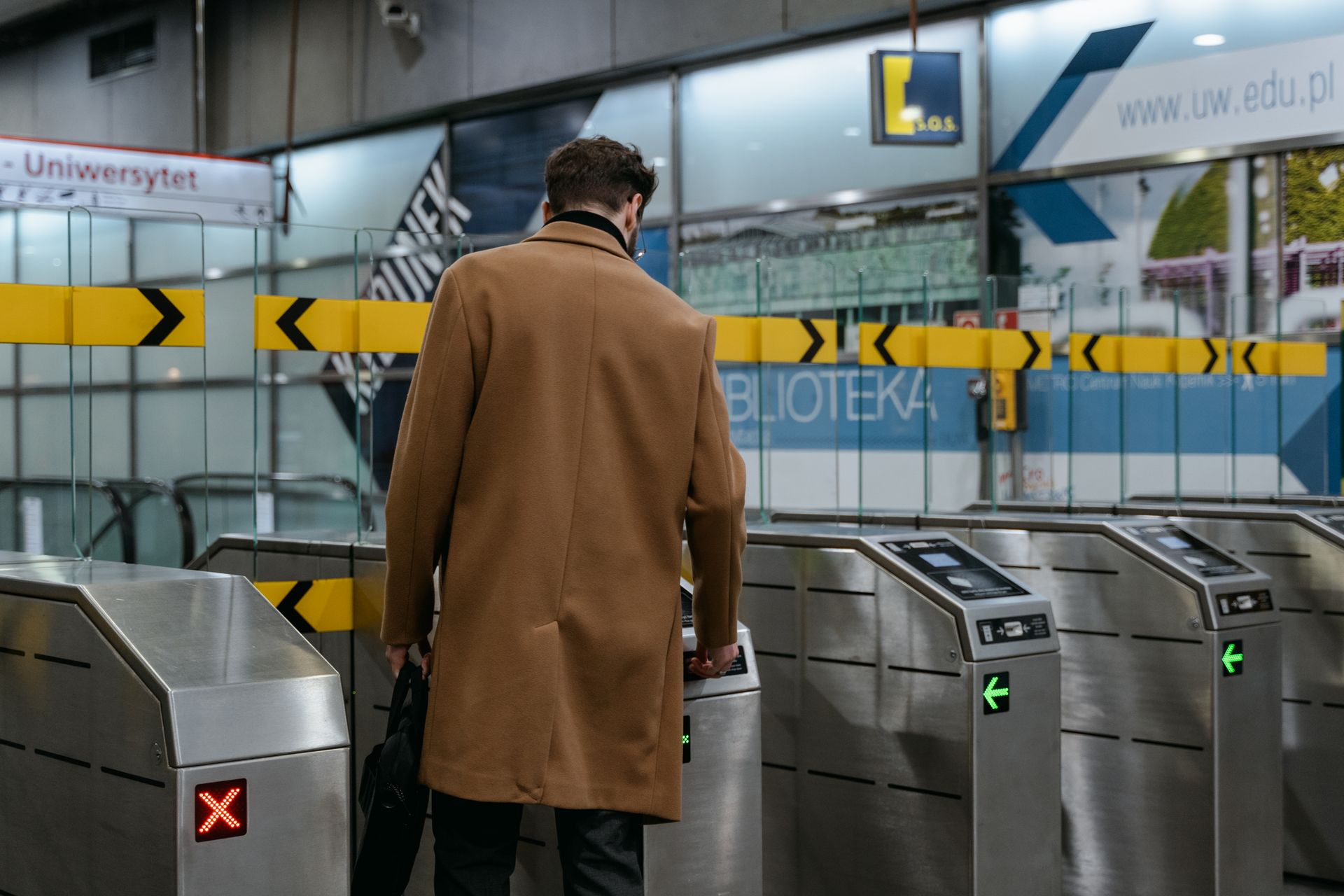 Commuter passing through electronic stainless steel turnstile gates at an underground transit metro station.