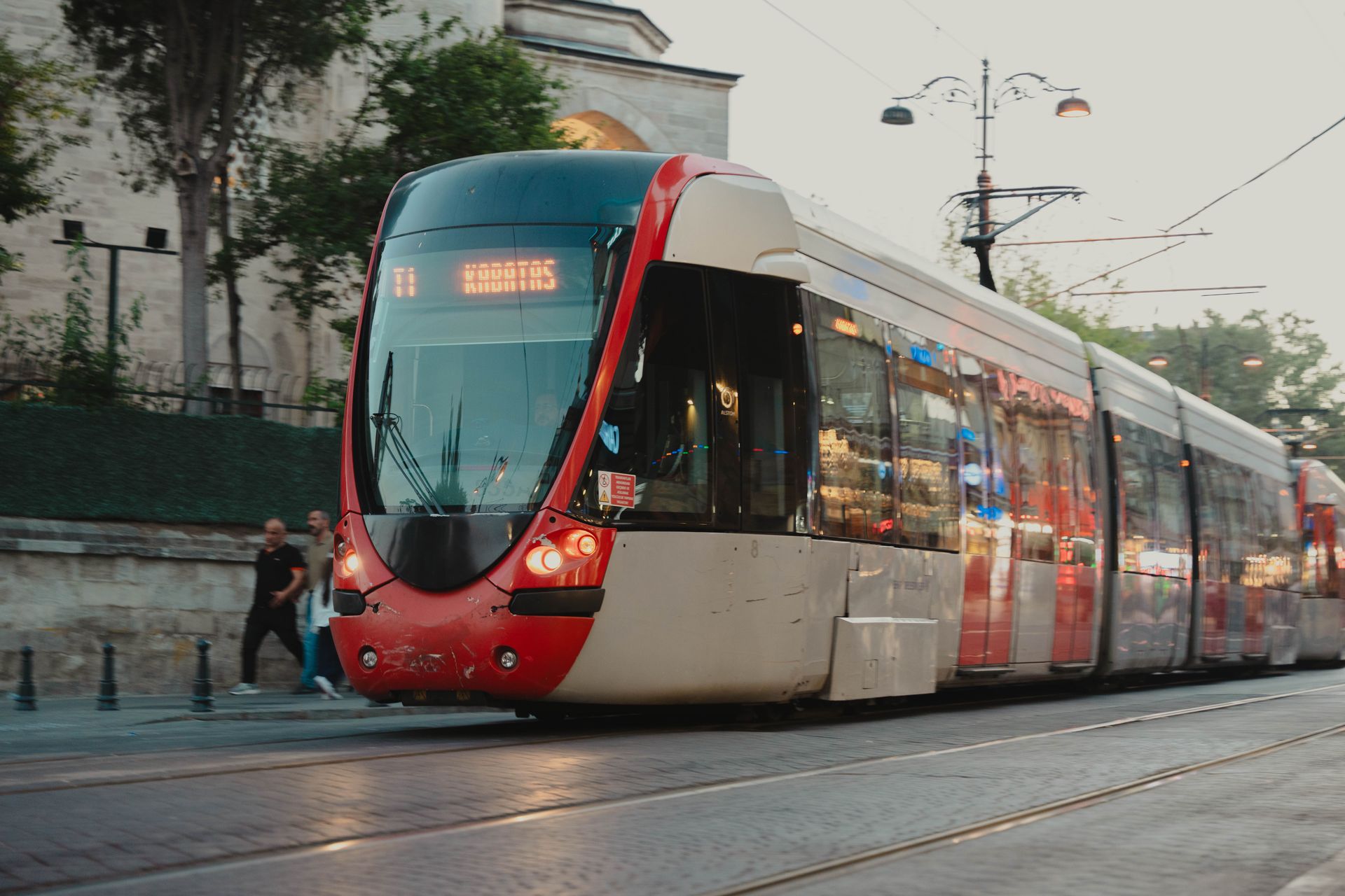 Modern red municipal streetcar traveling along track rails through Istanbul's historic district against a warm sunset.