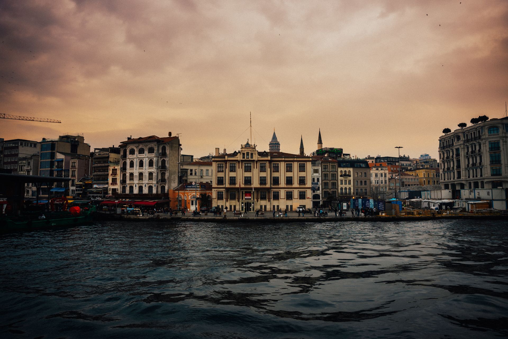 Historic stone facades and heritage buildings along the vibrant Karaköy waterfront district in Istanbul at dusk.