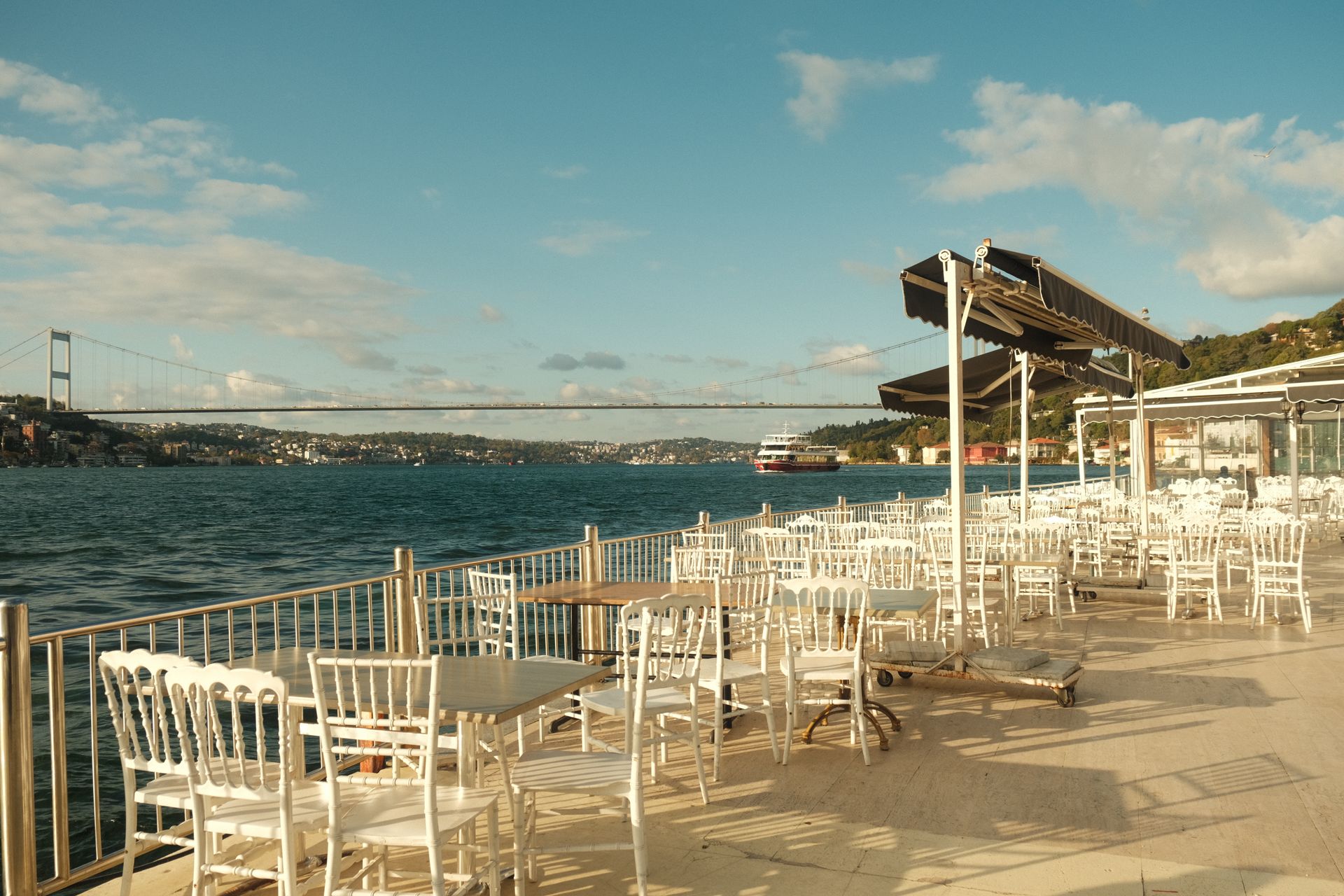 Upscale outdoor terrace restaurant overlooking the Bosphorus strait and suspension bridge along Kuruçeşme shoreline.