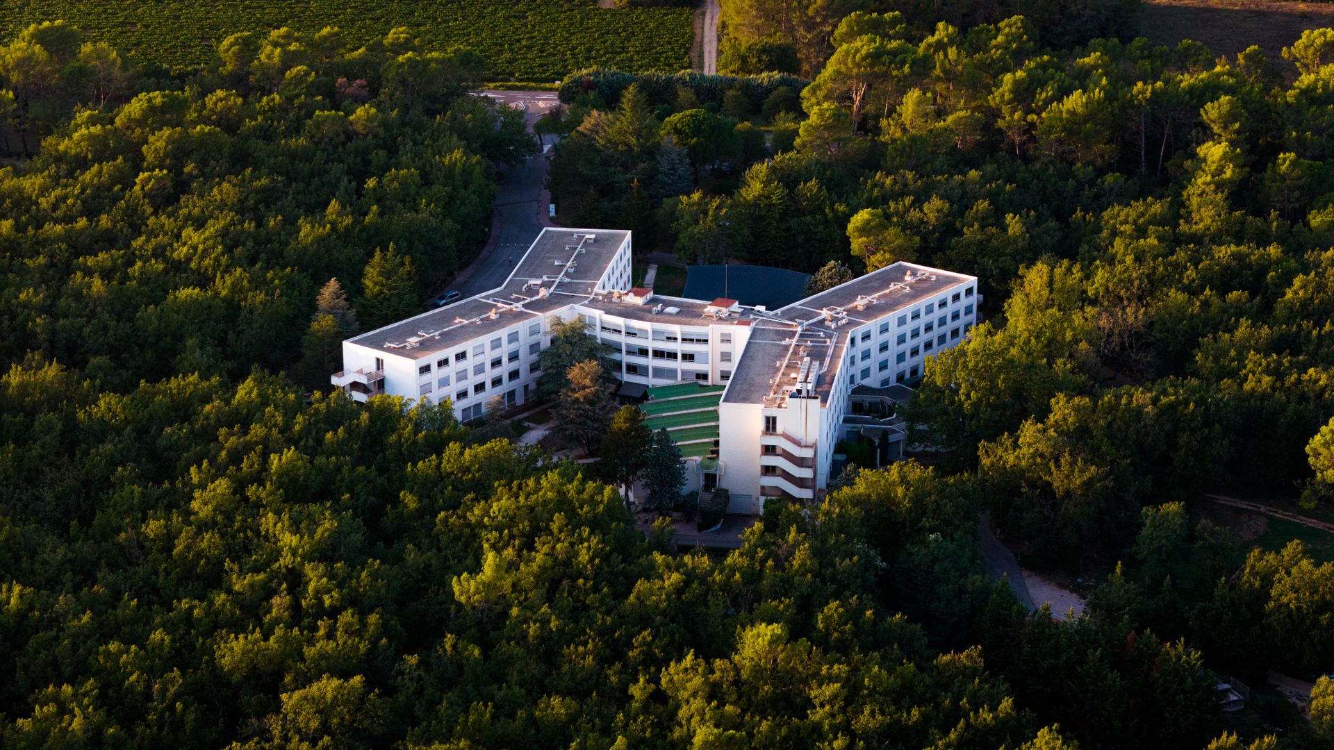 Aerial view of a contemporary hotel complex nestled within a lush green forest landscape.