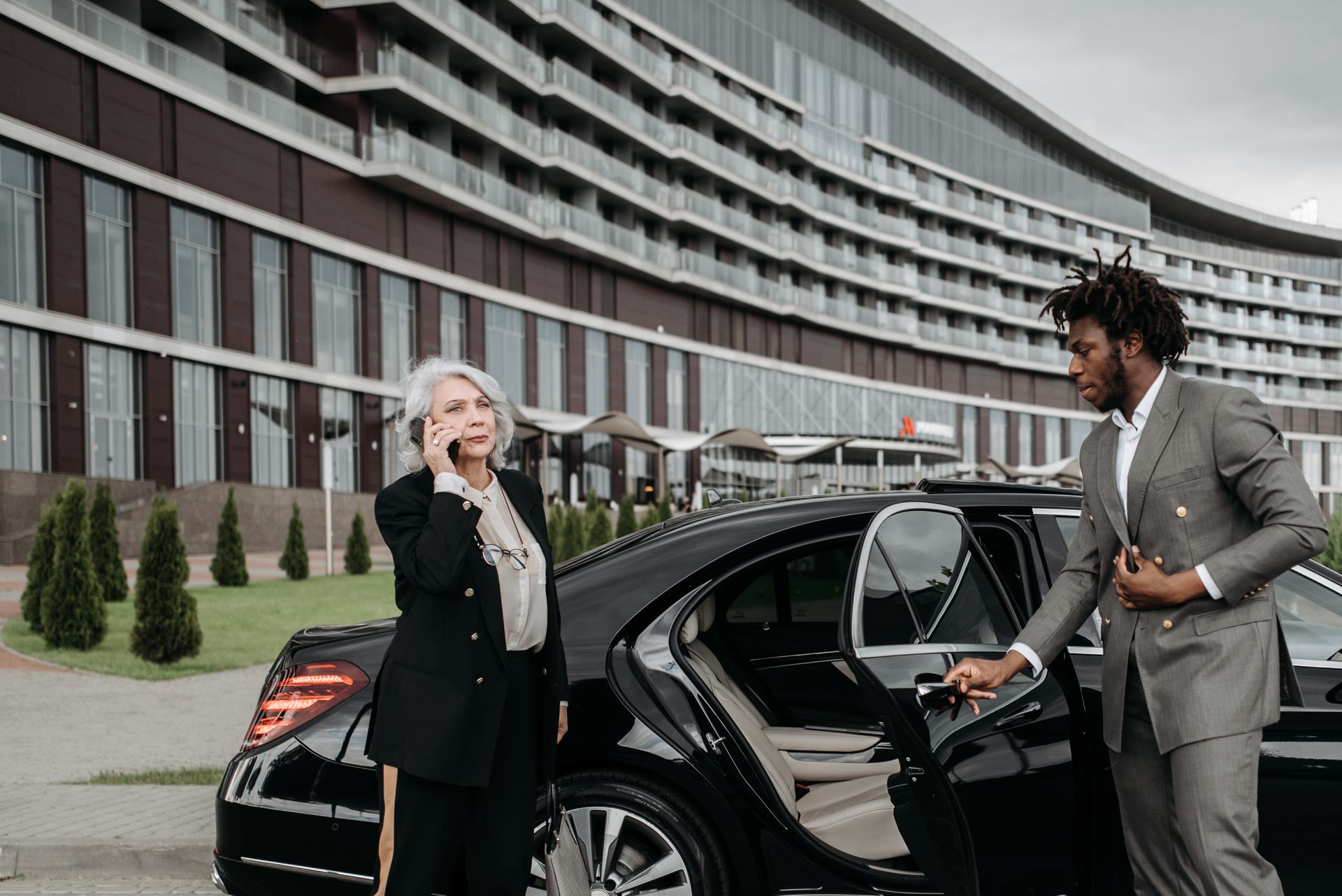 Professional chauffeur in formal suit courteously opening the rear passenger door of a luxury private transfer vehicle.