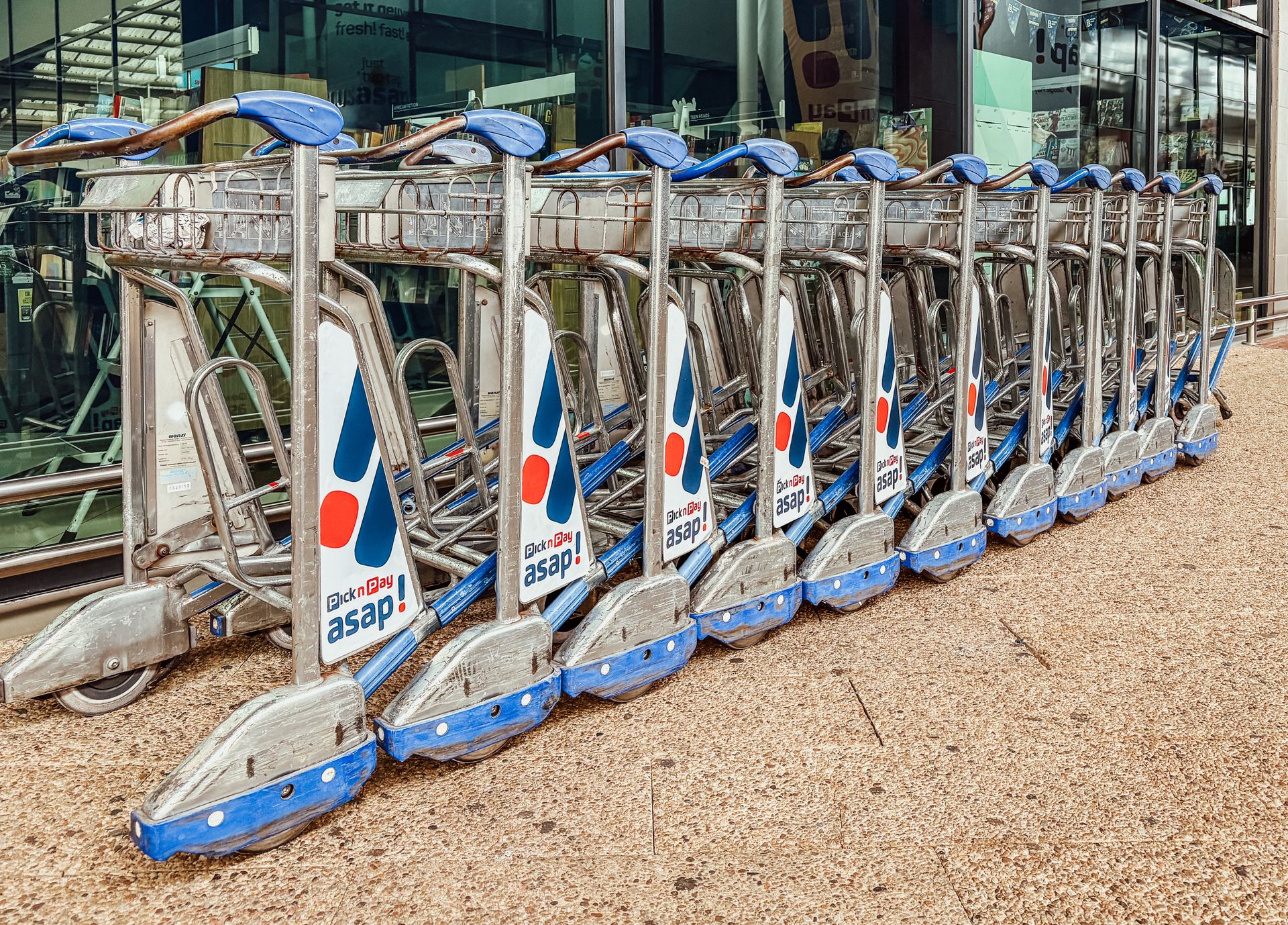 Organized row of stainless steel airport luggage trolleys and baggage carts ready for passenger transit outside the terminal.