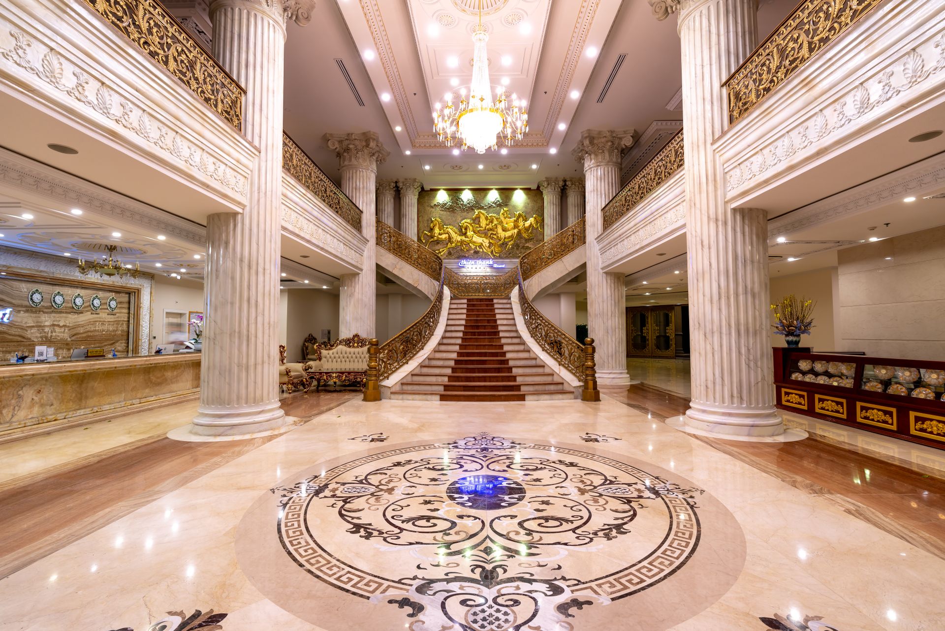 Opulent luxury hotel foyer featuring a grand marble staircase, polished floors, and a crystal chandelier.