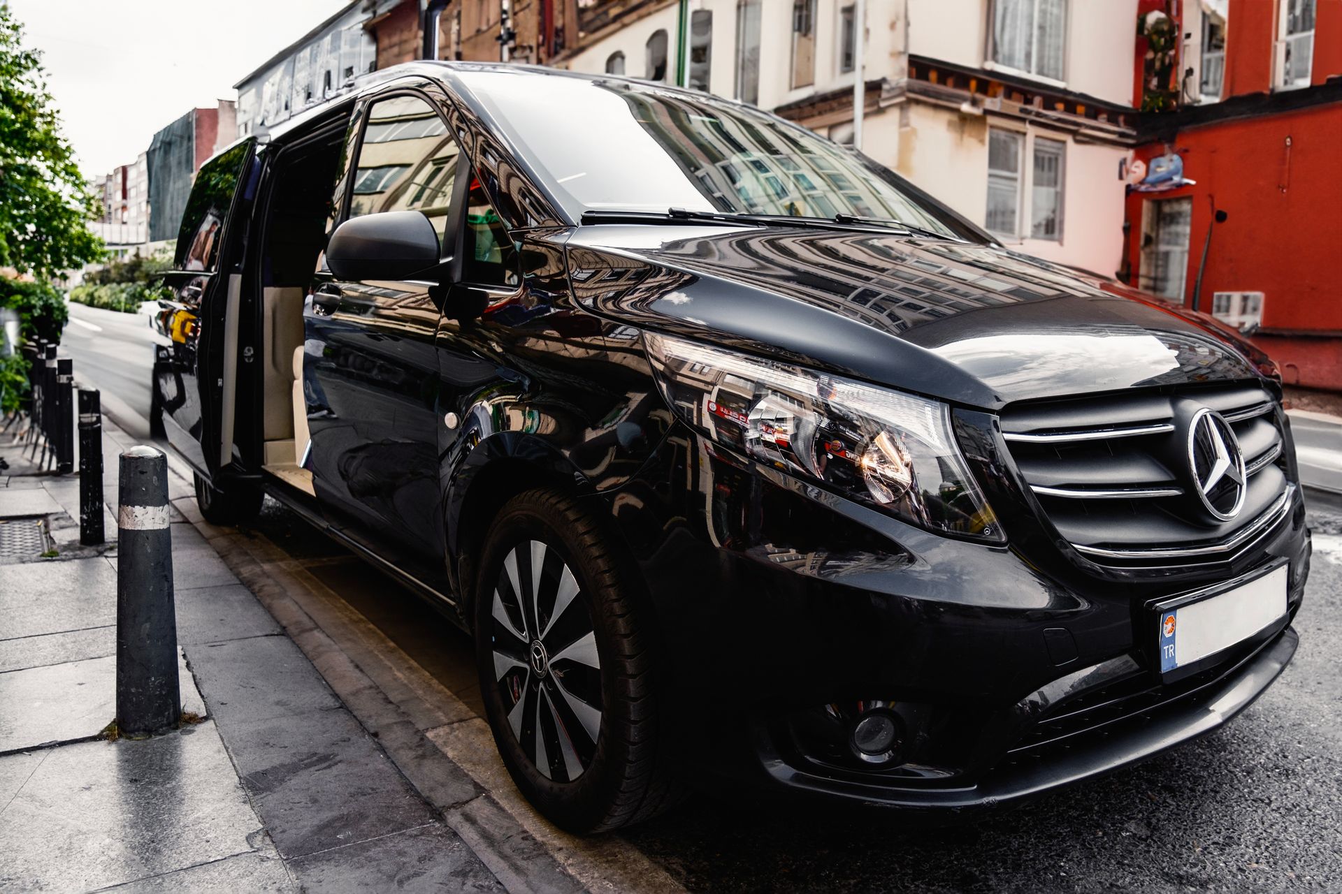Executive black Mercedes-Benz V-Class VIP transfer minivan parked curbside with sliding passenger door open for boarding.