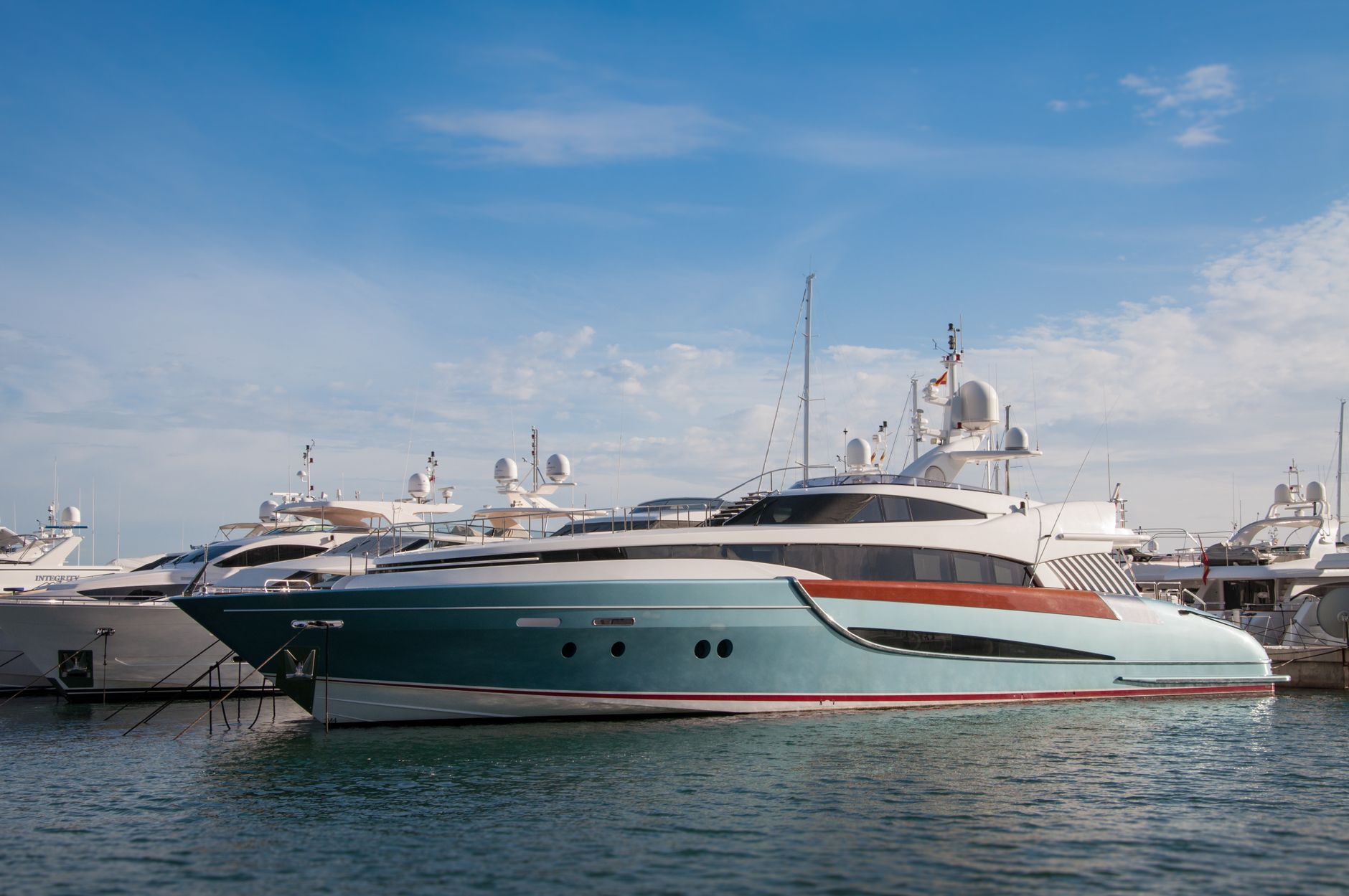 Pristine luxury yachts and sailboats moored at a modern marina harbor under sunlight.